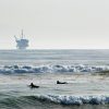 Surfers wait for waves with an offshore drilling platform in the distance in Santa Barbara, CA. Photo: Berardo62, Flickr CC.